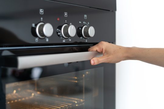 Cropped view of woman holding hond on modern built in oven handle and opening glass door, standing in kitchen