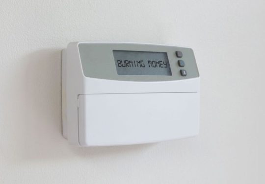 Vintage digital thermostat hanging on a white wall - Covert in dust - Burning money